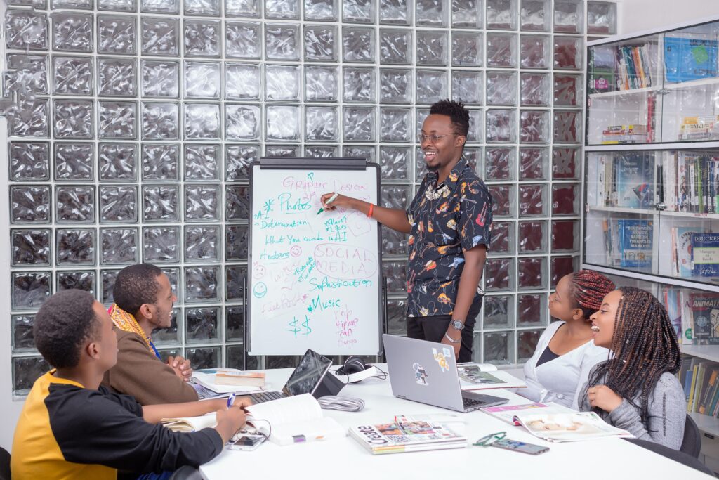 a man standing in front of a whiteboard with people around him discussing about E-Commerce tools