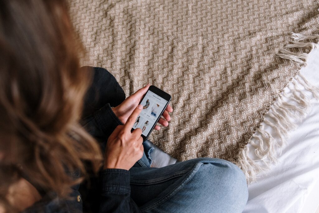 a woman sitting on a bed using a phone, browsing on online shopping store