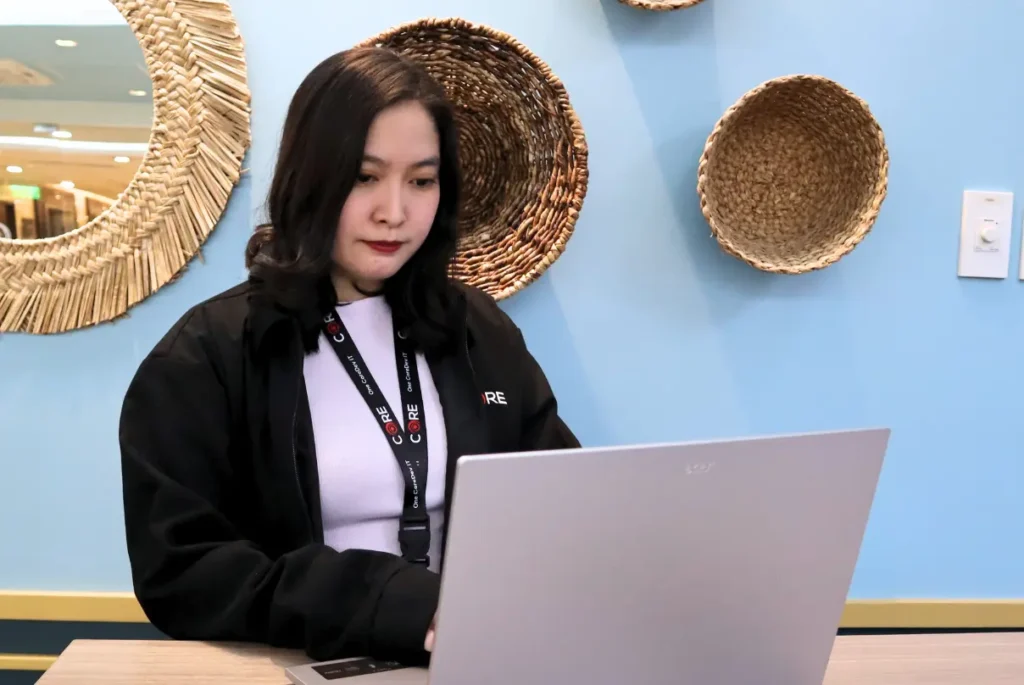A woman seated at a table, focused on her laptop, exploring options for choosing an employer of record.