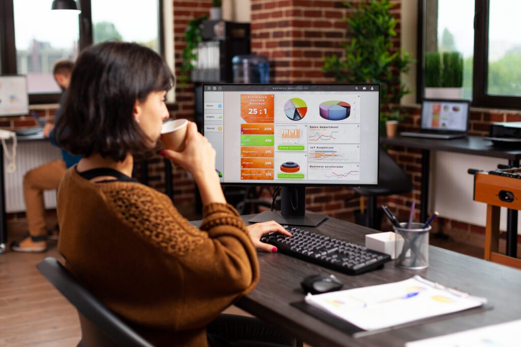 businesswoman holding cup of coffee, analyzing graphs, typing marketing strategy while working as a data analyst in the company project\s