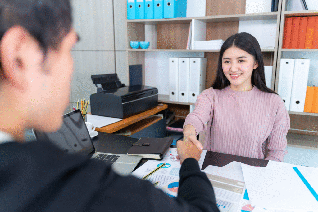 A woman and a man shake hands at a desk, symbolizing a partnership focused on EOR cost saving strategies.