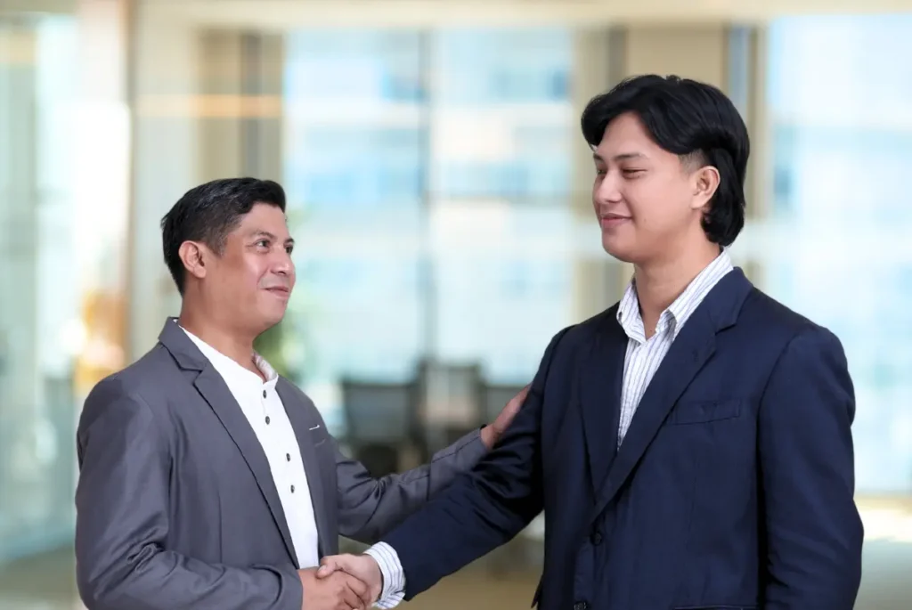 Two men shaking hands in an office, symbolizing collaboration in the project management life cycle.