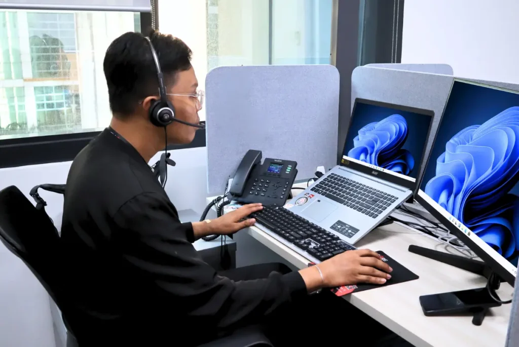 A man with headphones sits at a desk, focused on two computers, utilizing time tracking software for his small business.