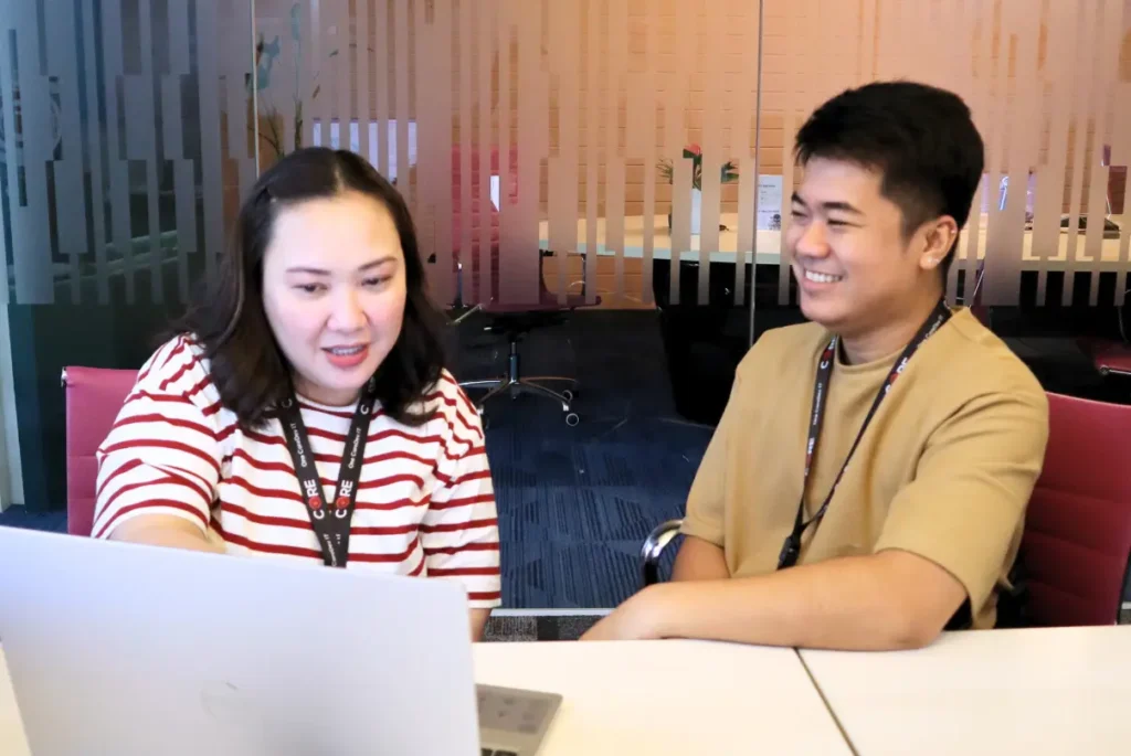 Two people seated at a table, collaborating on a laptop to analyze different types of recruitment processes.
