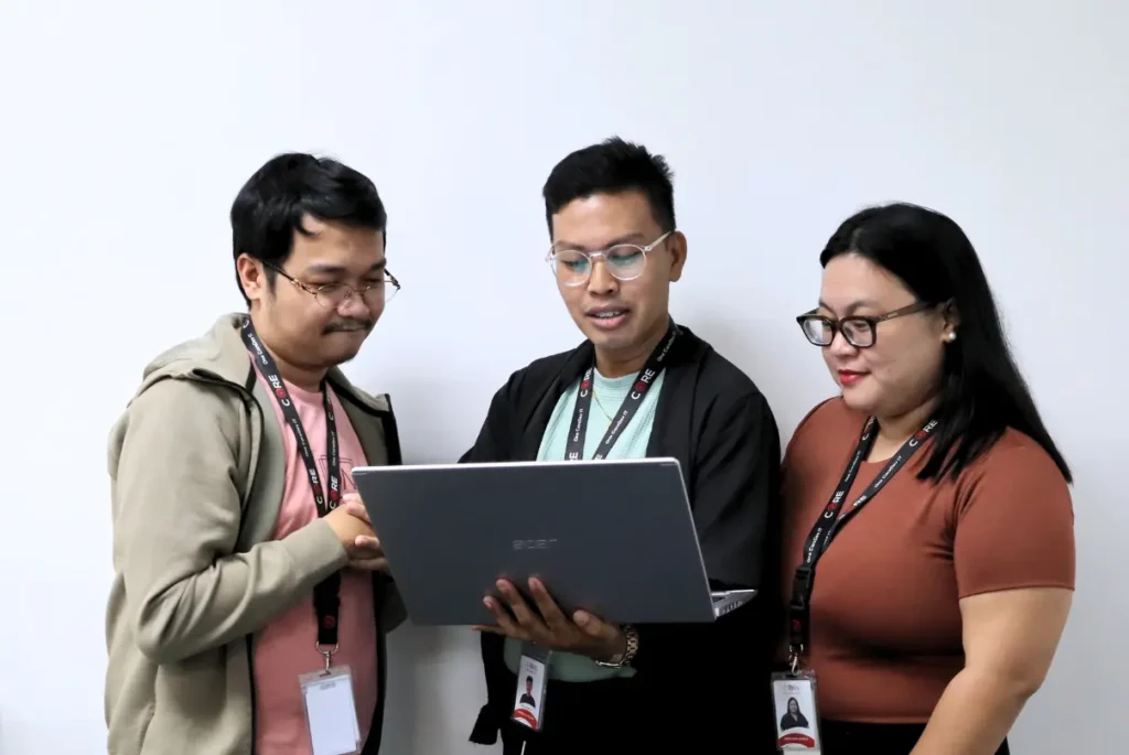 Three people gather around a laptop, strategizing on effective patient recruitment for clinical trials.