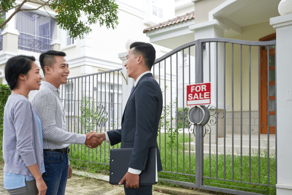 real estate employee shaking hands with two couple customers in front of a house