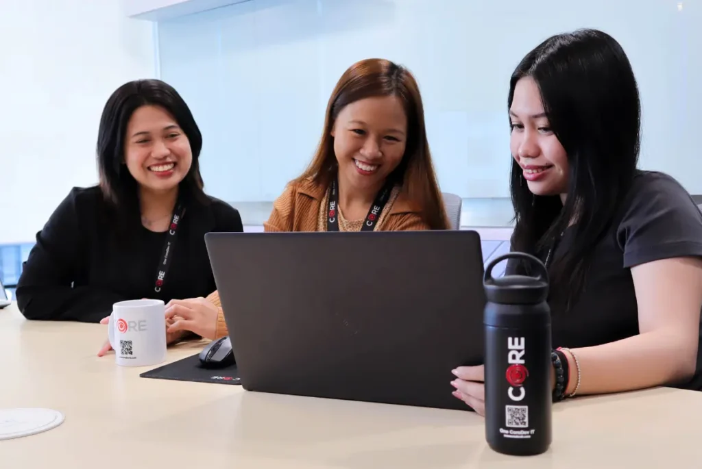 Three women engaged in discussion at a table, collaborating on a laptop for remote education in HR management.