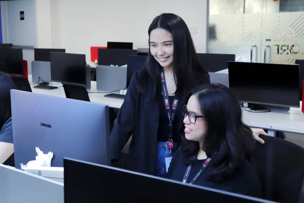 Two women collaborate on computers in an office, focusing on EdTech global talent acquisition strategies.