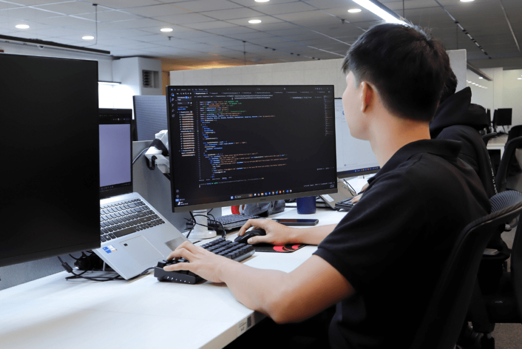 A man seated at a desk, working on two monitors, representing eLearning Managed IT Services.