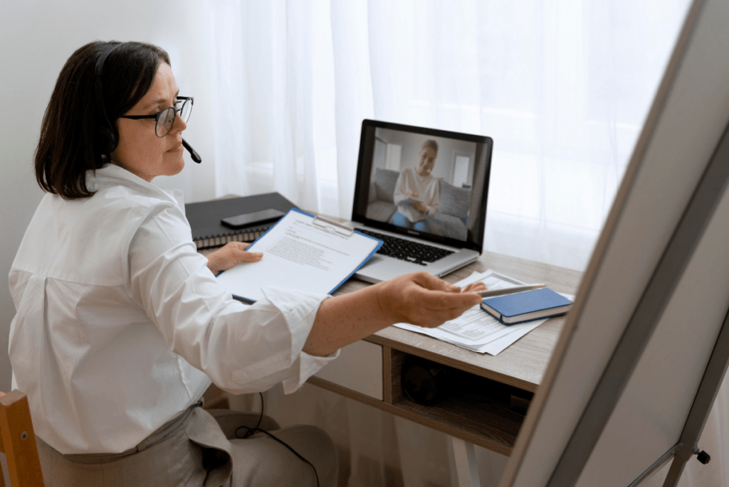A woman working as a remote real estate assistant, sitting at a desk with a laptop and a pen in hand.