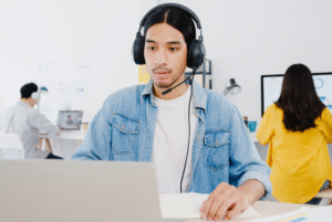 A man with headphones sits at a desk, focused on a laptop, representing the call center evolution in the Philippines.