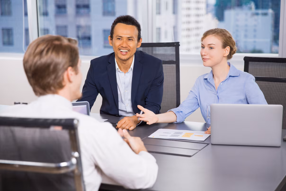 Three business professionals discussing HR managed services at a table in a modern office setting.