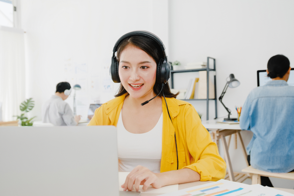 A woman in a headset sits at a desk with a laptop, engaged in e-commerce customer service.
