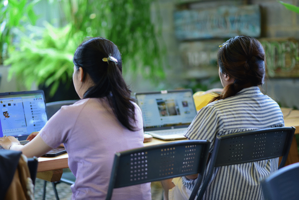 Two women seated at a table, working on laptops, discussing mandatory benefits in the Philippines.