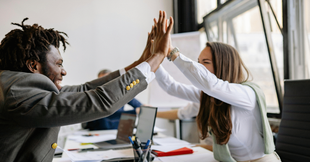 Two colleagues high-fiving in an office, symbolizing teamwork and positive employee retention strategies.