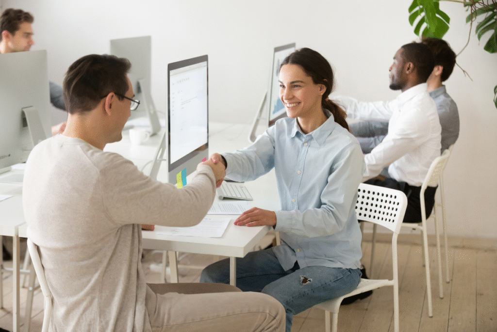 A man and woman shake hands in front of a computer, symbolizing a professional agreement in HR outsourcing in the Philippines.