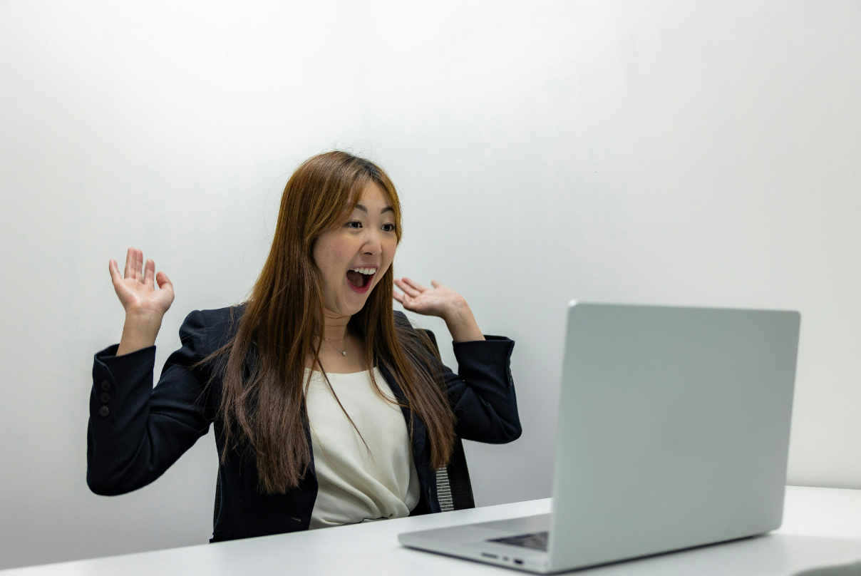 A woman in a business suit raises her hands while sitting at a desk, embodying a remote-first work culture.
