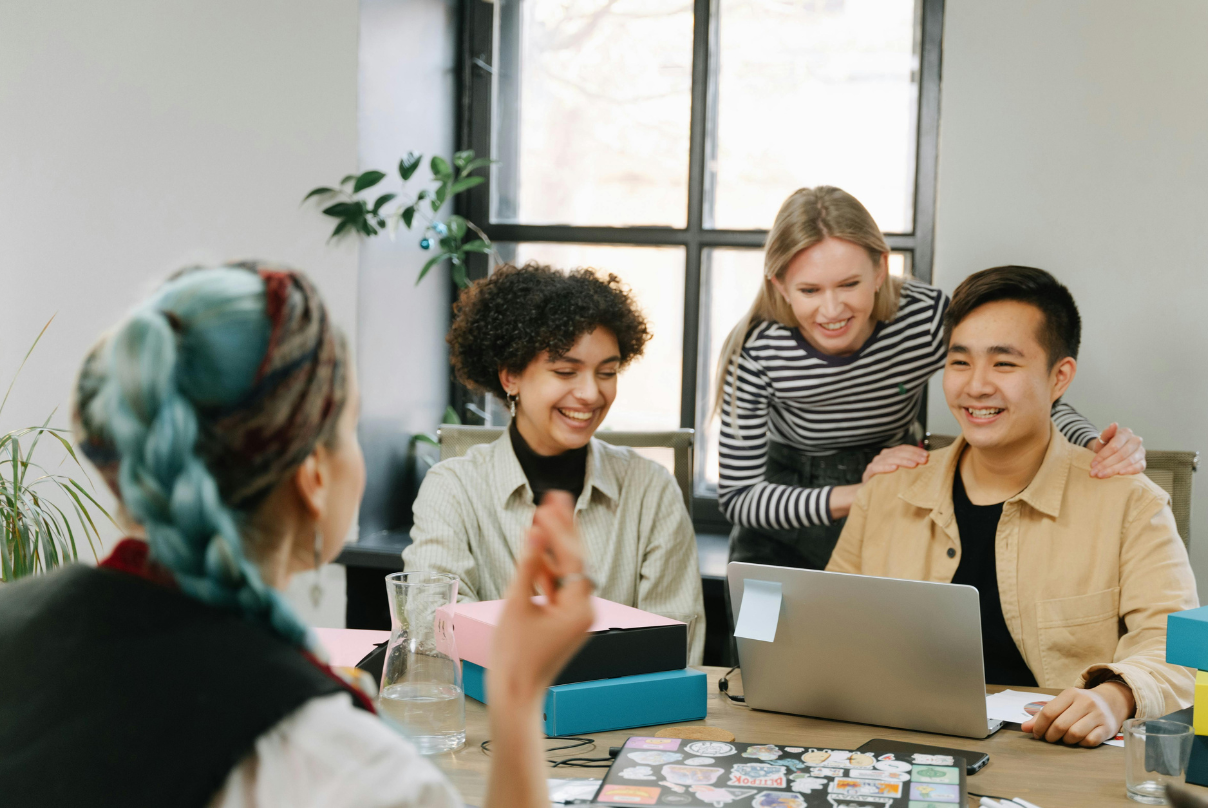 A diverse group of professionals collaborates around a table with a laptop, reflecting IT-BPM workplace culture.