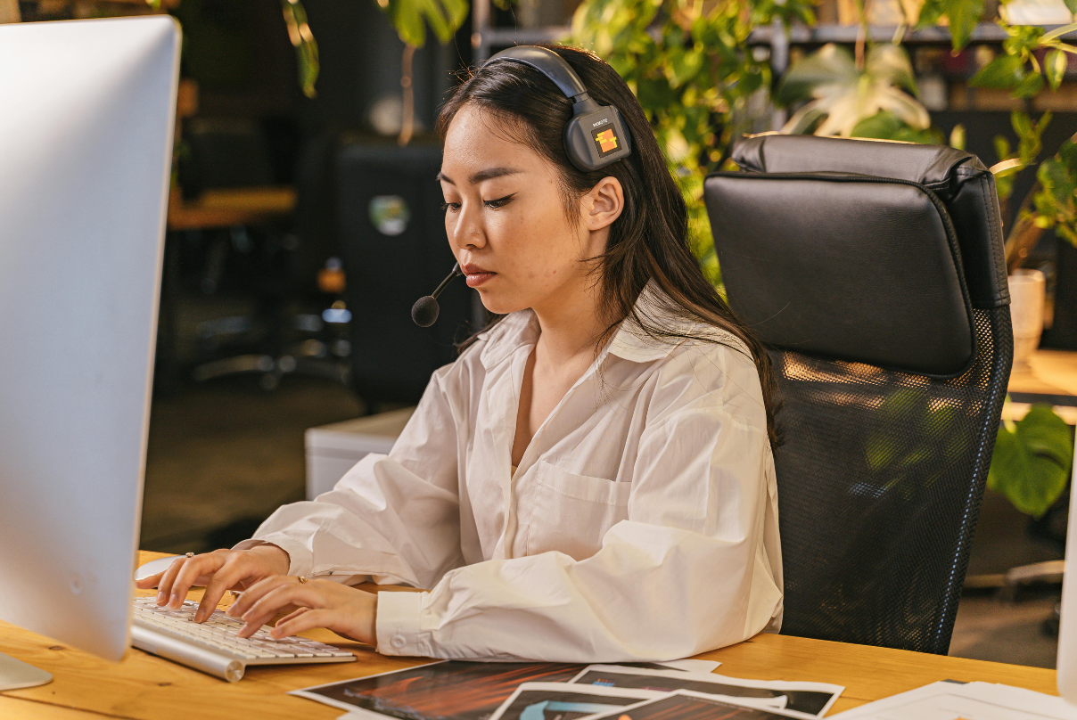 A woman wearing headphones types on a computer, representing a remote employee experience.