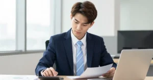 Offshore staff accountant reviewing financial documents at a desk with a calculator and laptop.